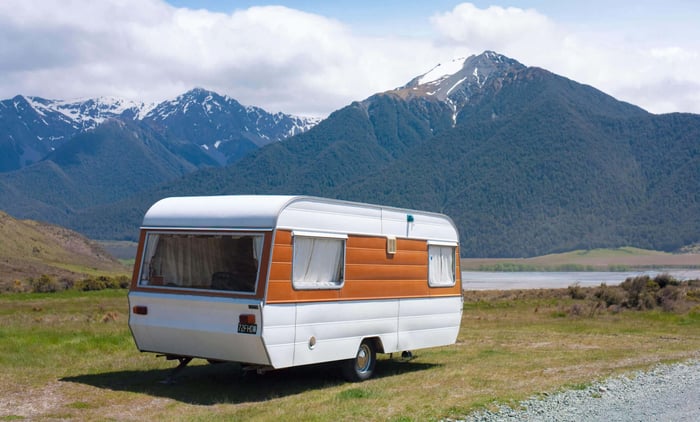 Une vieille caravane de couleur orange et blanche située dans un paysage de montagnes rocheuses