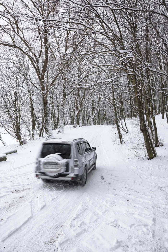 Un 4x4 roulant avec ses pneus cloutés sur une piste enneigée dans une forêt