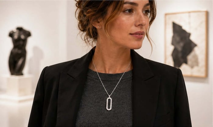 Woman wearing a long pavé diamond paperclip pendant with a charcoal knit and black tailored jacket in an art gallery
