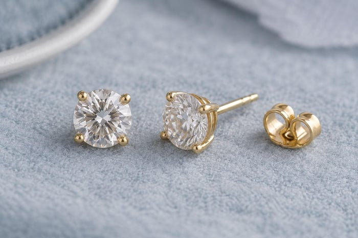A matching pair of round diamond studs in yellow gold, with the post and back visible beside one earring.