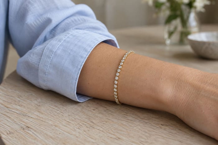 A slender yellow-gold diamond tennis bracelet worn beside the cuff of a pale-blue shirt.
