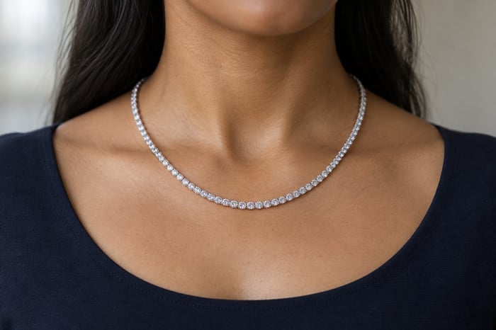 A fine diamond tennis necklace resting above the neckline of a dark-navy top.