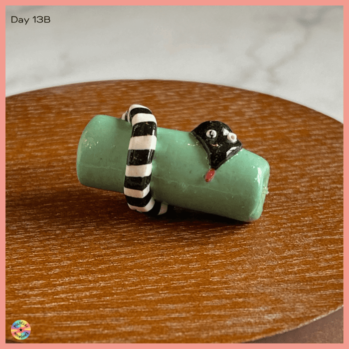 A black and white polymer clay snake on a green bead.