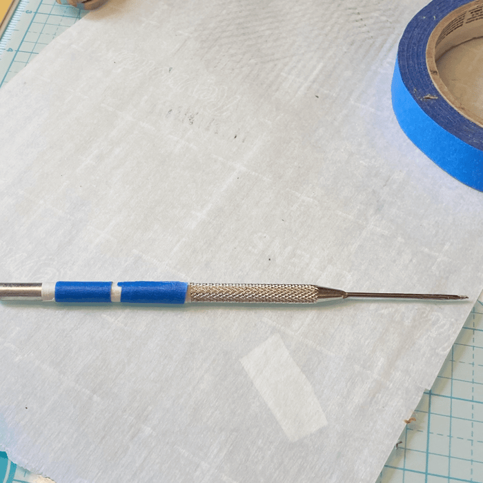 Photo showing parchment paper secured around the handle of a needle tool with blue painter's tape