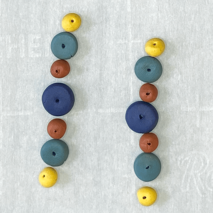 Baked polymer clay beads lined up in earring order.  Temperature flares in the oven darkened the clay color.