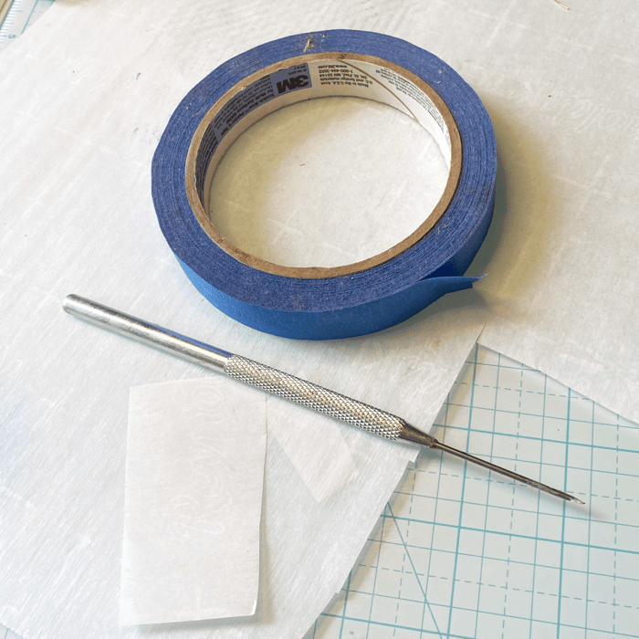Photo of parchment paper, blue painter's tape and a needle tool