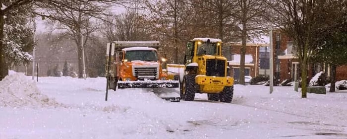 Two snowplows plowing a residential street during a snowstorm.