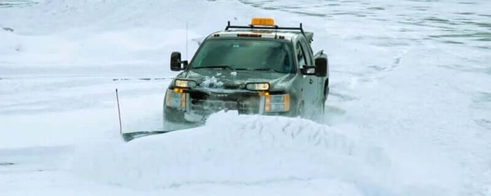 GMC Pickup truck fitted with a snowplow pushing large snow bank in a snowy parking lot.