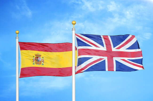 Photo of a Spanish flag and the Union Jack flag flying in Spain with a blue sky background.