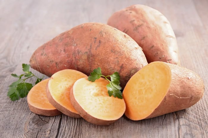 A combination of whole and sliced sweet potatoes displayed on a rustic wooden table.