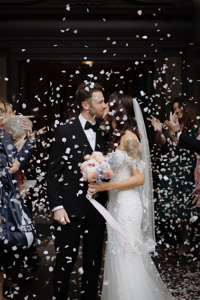 A bride and groom kiss under a shower of circle and heart shaped wedding confetti