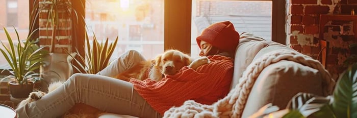 Young adult relaxing on a sunlit loft sofa with their golden retriever, cozy and content—feel better, THiNK LiKE A DOG.