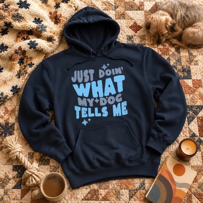 Black crewneck sweatshirt with blue “Just Doin’ What My Dog Tells Me” graphic, styled flat lay with dog toys, iced coffee, denim, and retro props.