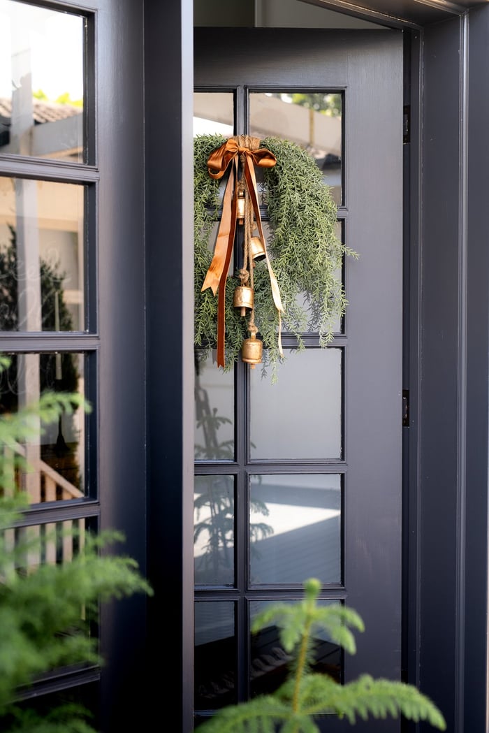 Navy blue door with rosemary wreath with bells and ribbon.