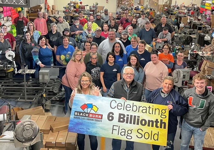 Blackburn team in warehouse holding 6 billion flags celebration sign