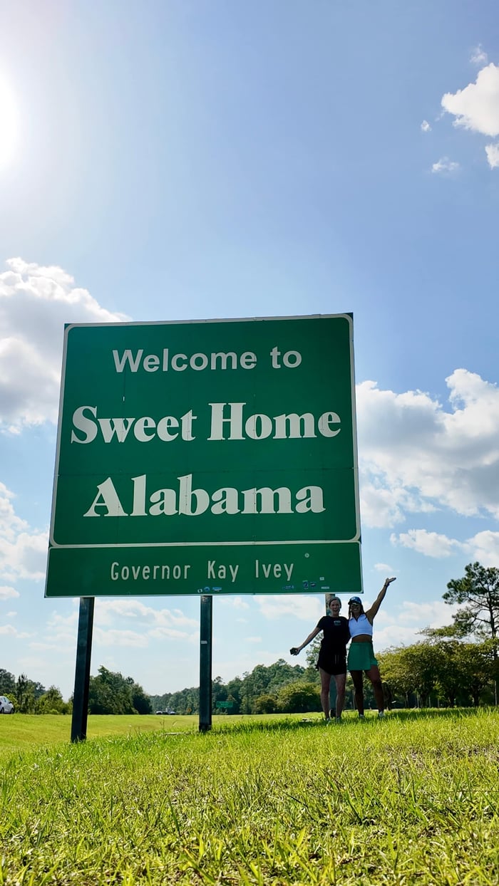 A photo of teh alabama border sign with Two women standing by the sign.