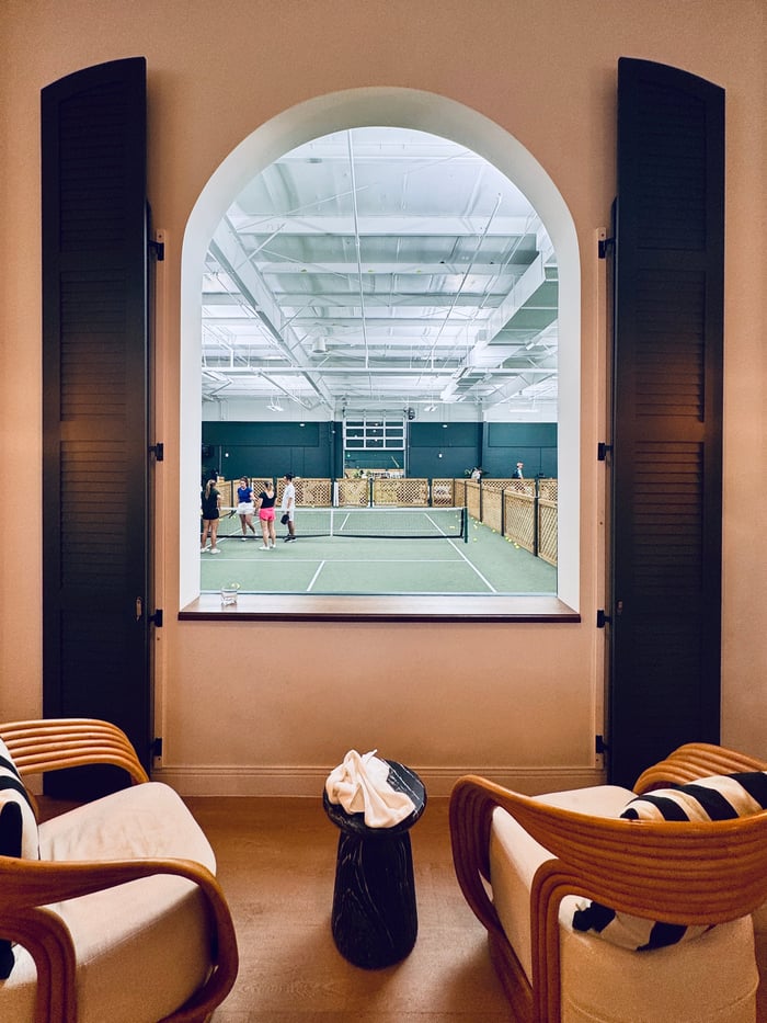 View of indoor pickleball courts from two chairs in a lounge overlooking courts through an archway at St. Pete Athletic.