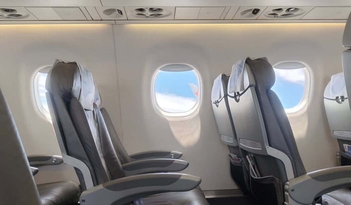 飛機內部空座位與窗外藍天,用以說明大容量背包算隨身行李時,必須符合放入頭頂置物箱的尺寸規範。