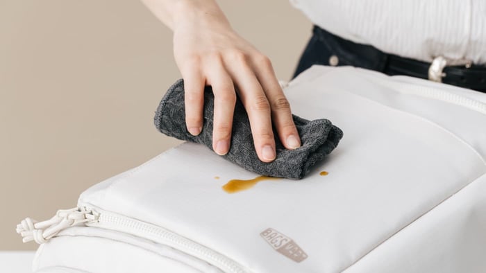 使用濕抹布擦拭白色款 Bagsmart 後背包表面的咖啡污漬，展示 TPU 機能布料防潑水與便於後背包清潔的物理特性。