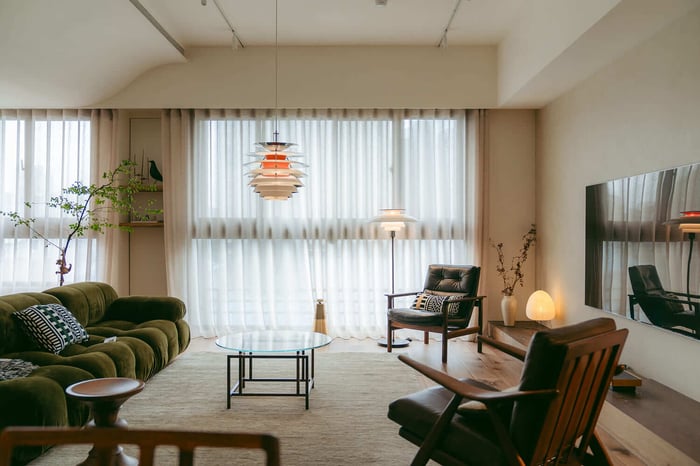 寬敞的中世紀現代風格客廳全景,核心是綠色 B&B Italia Camaleonda 沙發,上方懸掛著經典的 Louis Poulsen PH Artichoke 吊燈,窗邊配有 PH 落地燈,整體呈現洗鍊的柚木居家氛圍。