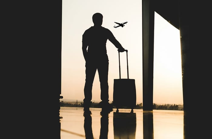 機場航廈內拉著行李箱準備登機的商務旅客剪影,探討出差族如何挑選符合登機標準的大容量「旅行後背包」。