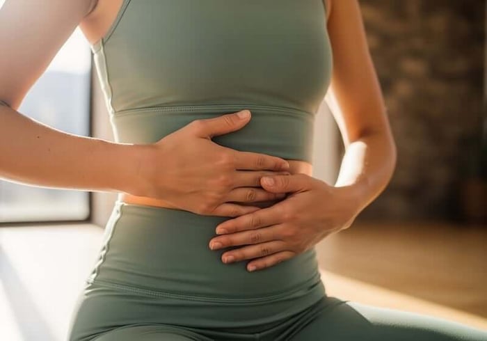 穿著綠色運動服的女性雙手撫摸腹部,苦惱久坐造成的小腹怎麼瘦並尋求最快改善體態的方法。