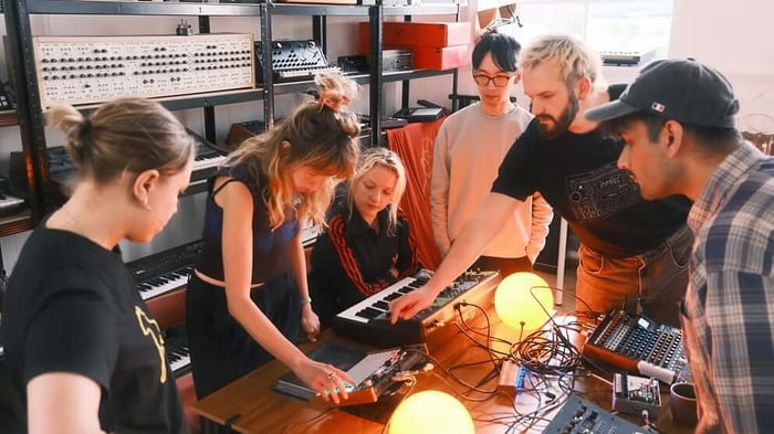 A group of particpants gathered around a synthesiser at GLOSS
