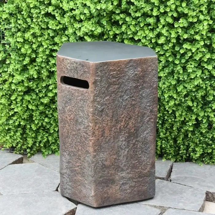 Elementi Columbia 15" Seat or Propane Tank Cover, a textured rectangular stool with a handle cutout, shown outdoors against a green foliage wall and stone pavers.
