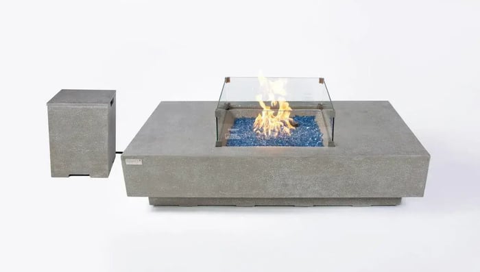Light grey concrete square fire table with glass wind guard and separate tank cover on white background.