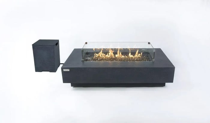 A dark grey rectangular fire table with a glass wind guard and lit flames, alongside a separate dark grey tank cover, on a white background.