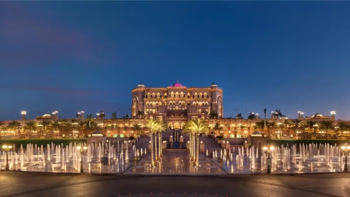 A breathtaking view of a luxurious palace hotel, adorned with intricate details and shimmering lights, reflecting in the waters of a grand fountain.
