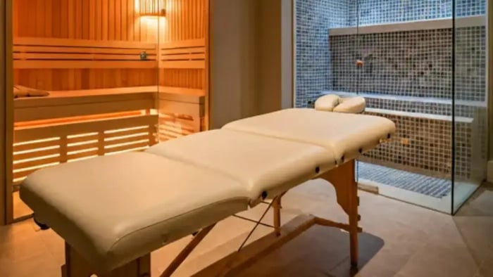 A luxurious, spa-like room with a massage table, sauna, and steam room. The room is bathed in soft, warm light, creating a serene and inviting atmosphere.