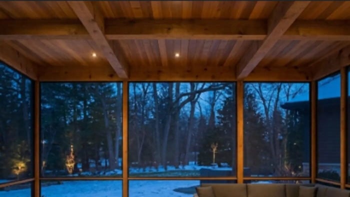 A luxury 400-square-foot screened porch in Lake Forest featuring custom cedar tongue-and-groove ceilings, exposed timber framing, a deep sectional sofa, and floor-to-ceiling fine mesh screens overlooking a snowy winter landscape.