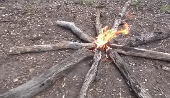 camp fire using star method. wood logs of various sizes are used with a kindle in the middle that has orange flames