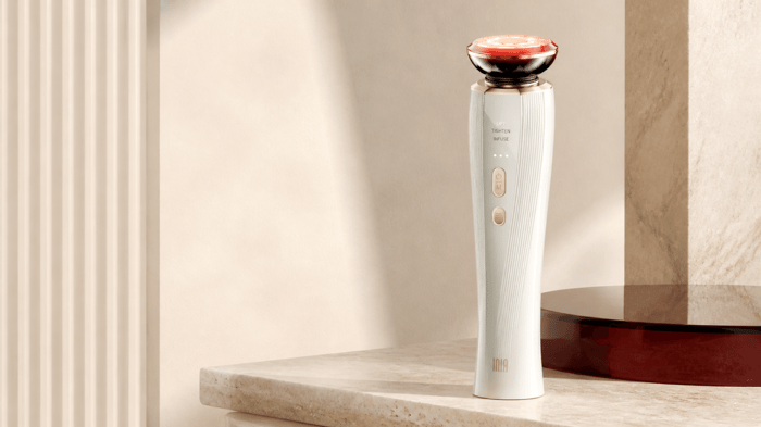 INIA FLARE Microcurrent Facial Device standing on a stone vanity with its electrode head illuminated