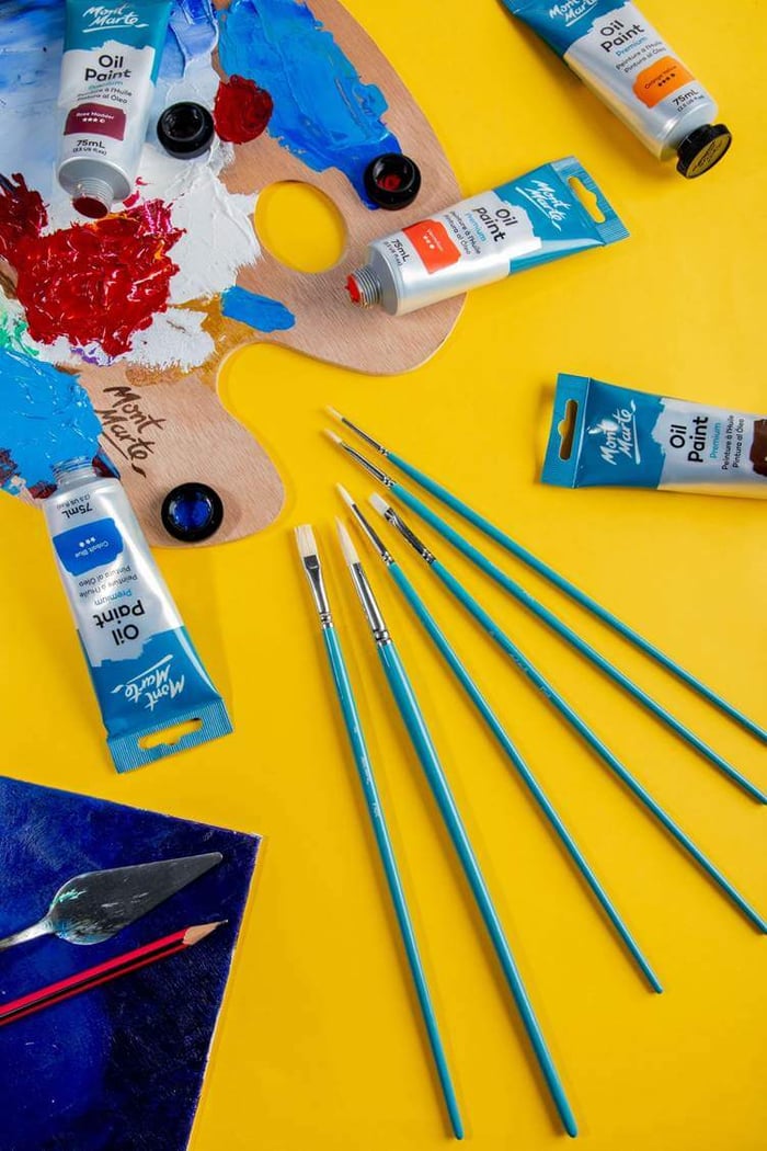 A bright photo of oil paints with a wooden palette and brushes next to it.