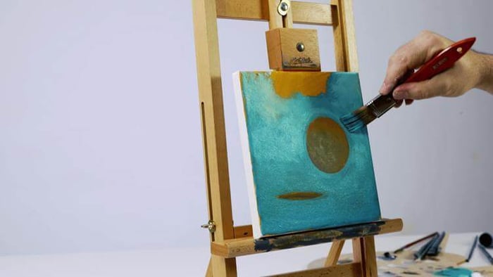 Hand painting an underpainting artwork on a wooden canvas with a red brush.
