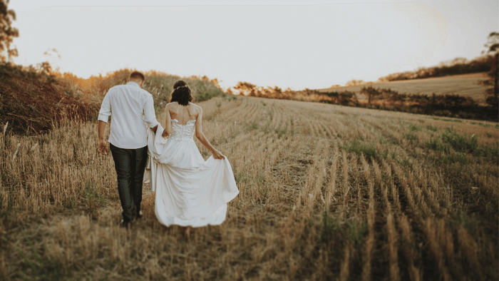 Bride and groom walking through a field in wedding attire, celebrating a sustainable wedding