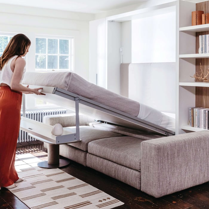 A woman demonstrating the transformation of the Tango Sofa wall bed from Resource Furniture, showing how to maximize space in a modern living room