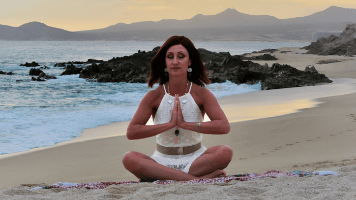 Sondra Dubas seated on the beach, with the ocean in the background, appearing calm and contemplative.