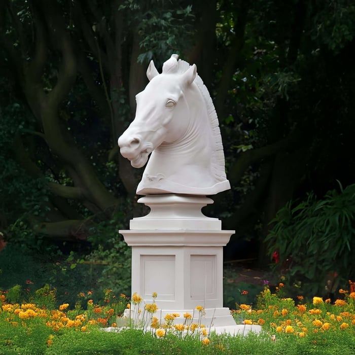 Classic white horse head statue on a pedestal, surrounded by marigolds in a shaded garden.