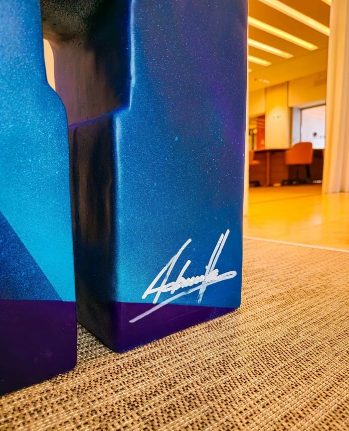 Close-up of the Giant Sculptures' Midnight Sunset Bear Sculpture - 165cm, an exclusive art collectible characterized by sharp angles and geometric shapes, adorned with a gradient of blue and purple hues. A white signature is visible on one of the surfaces, set against a plain white background.