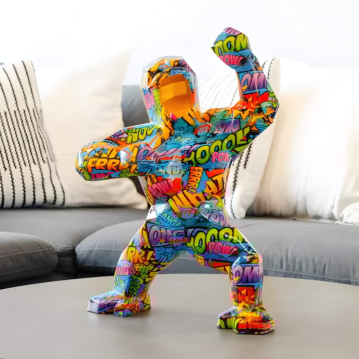 Vibrant geometric gorilla sculpture covered in comic-style text and graphics, posed with raised fists, placed on a coffee table in a modern living room.