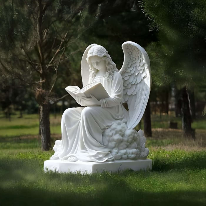 White angel statue reading a book, seated on a cloud-like base in a peaceful wooded garden.