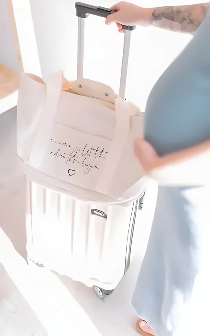 A white baby bag on top of a white suitcase, with a pregnant lady baby bump