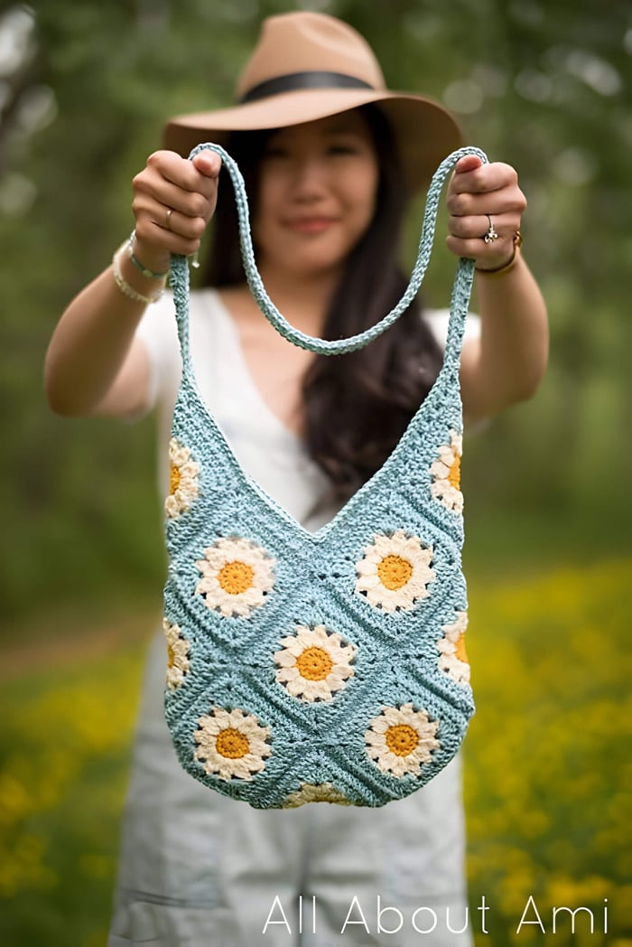 a lady in a brown hate and white t shirt holding a blue and white daisy crochet bag
