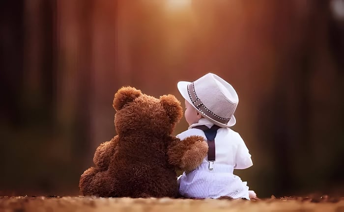 a child and a teddybear sat down together, the bear has its arm round the child
