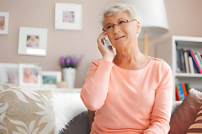 An older female in a pink jumper talking on the phone