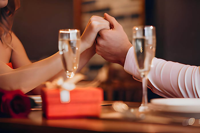 a couple holding hands over a restaurant table with flutes of champagne