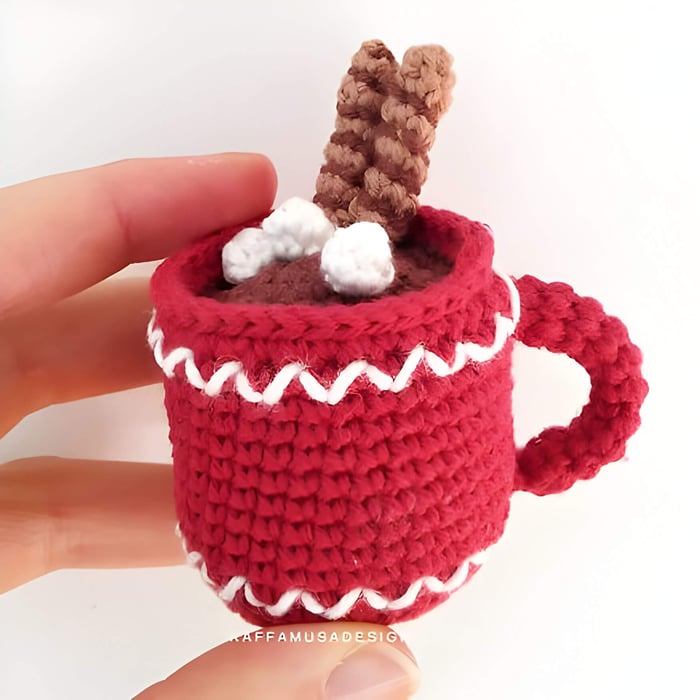a red crochet mug with crochet marshmallows and flake